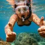 Woman snorkelling under water. Female swimmer with diving mask and snorkel giving thumbs up in sea.